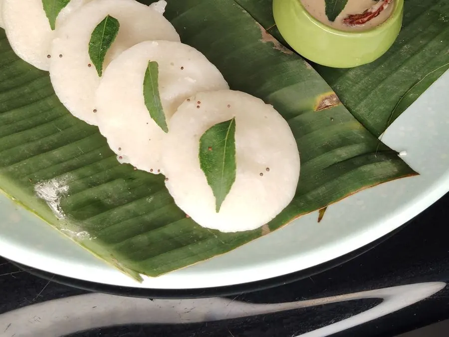 Soft idli on a banana leaf with sambar and coconut chutney