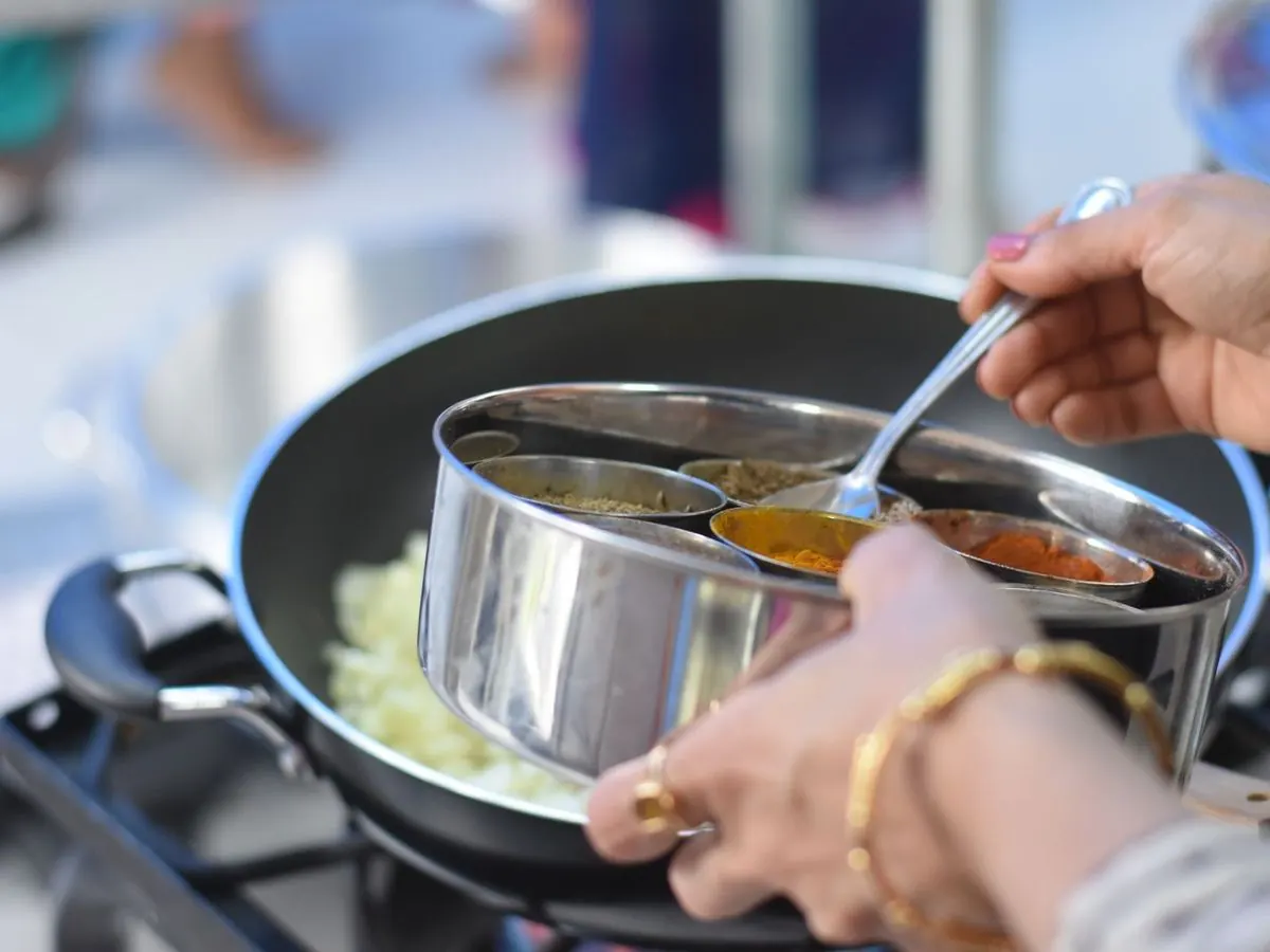 Hands adding spices from a masala box to a pan